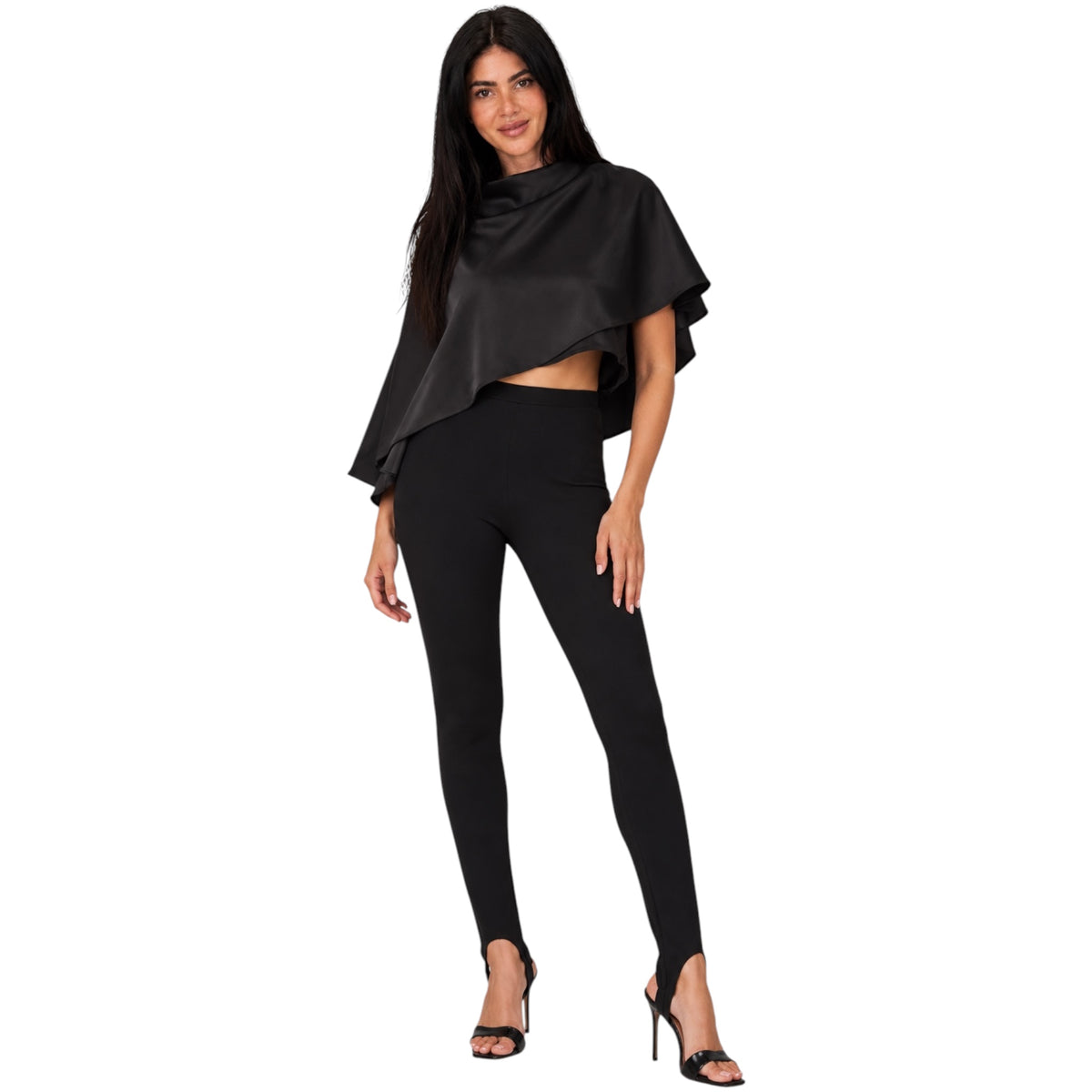 A woman modeling a black draped cape-style top and black leggings with black high-heeled sandals against a plain white background.