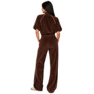 A woman wearing a matching brown velour tracksuit, viewed from behind, standing against a solid white background.