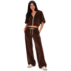 A woman modeling a brown velvet lounge set consisting of a cropped zip-up top with short puff sleeves and matching wide-leg drawstring pants, shown against a plain white background.