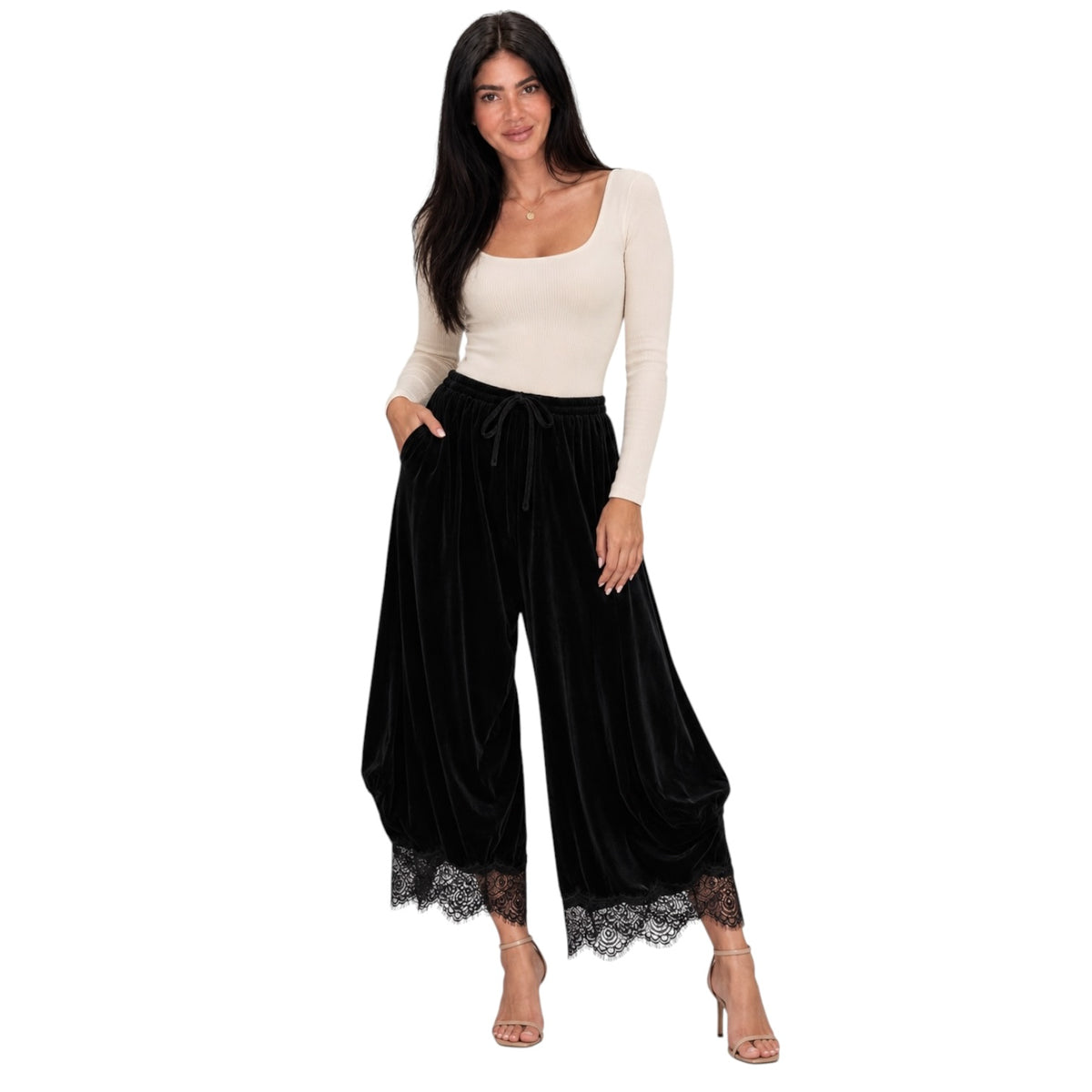 A woman modeling black velvet wide-leg pants with a lace hem, paired with a cream long-sleeve scoop-neck top, on a solid white background.