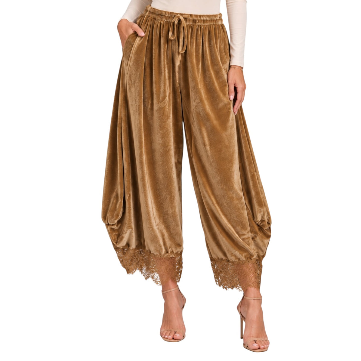 A model wearing wide-leg velvet harem pants in a warm camel brown color, styled with a cream long-sleeve top and nude high-heeled sandals against a plain white background.