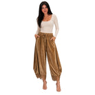 A woman modeling loose, harem-style pants in a warm brown velvet-like fabric with a drawstring waist and lace-up hems, paired with a cream long-sleeve top, against a plain white background.