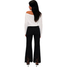 A woman shown from the back wearing a white off-the-shoulder long-sleeve top and black flared pants with lace detailing at the hem, against a plain white background.