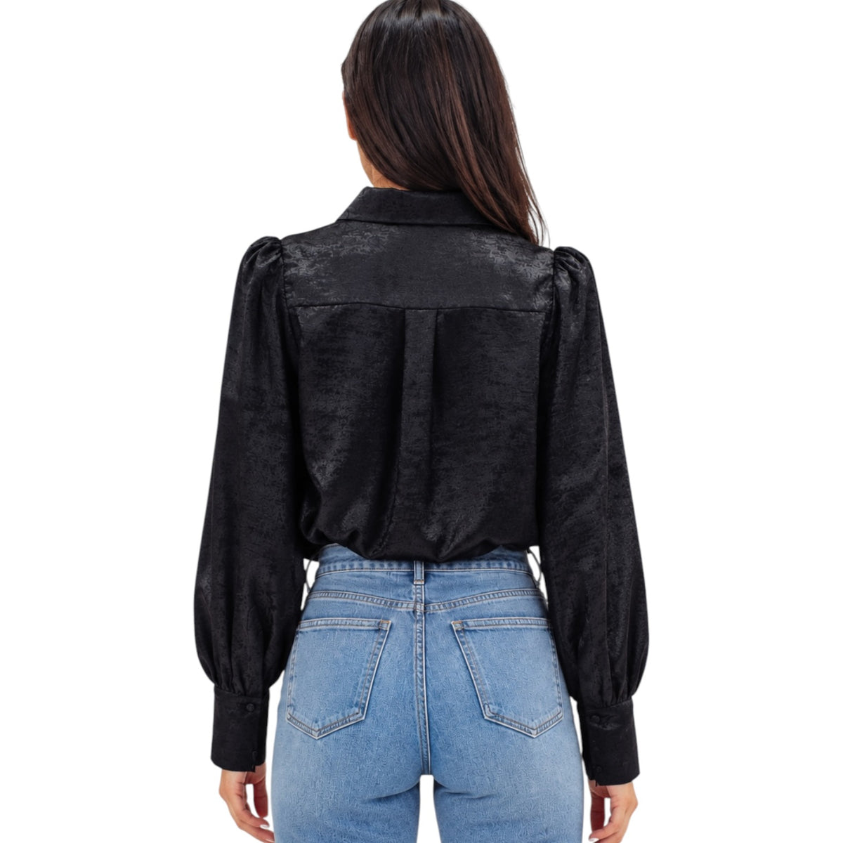 A woman viewed from the back wearing a black long-sleeve blouse with textured fabric and puffed shoulders, paired with light blue jeans, against a plain white background.
