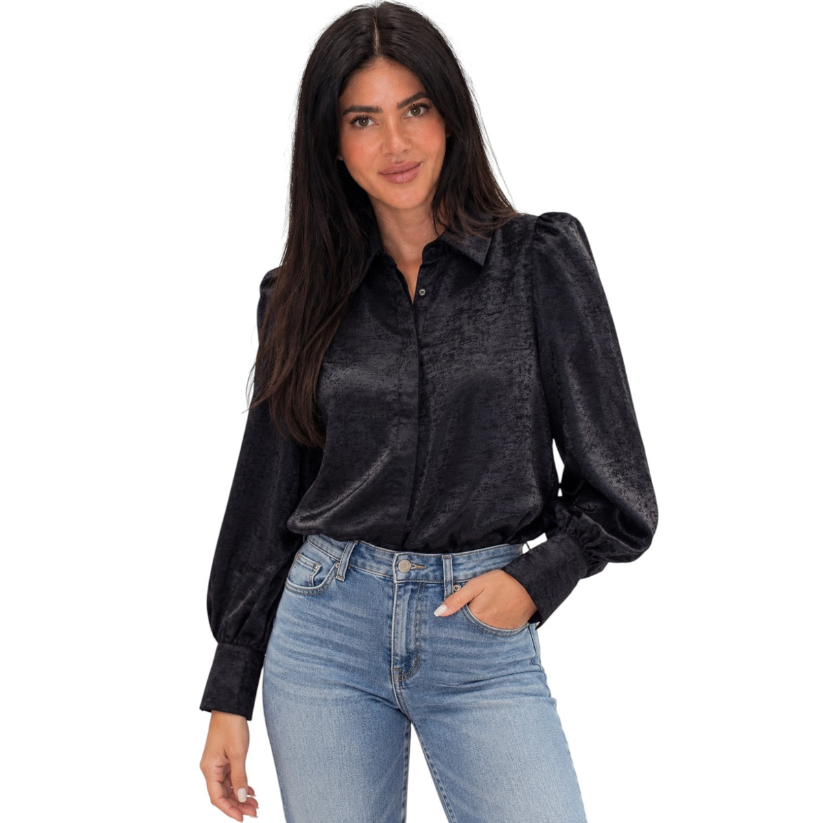 A woman modeling a black long-sleeve button-up blouse with textured, slightly shiny fabric and puffed shoulders, paired with light blue jeans, against a plain white background.