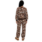 A model shown from the back wearing a matching brown floral sweatshirt and jogger pants set, featuring a dark brown base with pink, beige, and light blue floral patterns.
