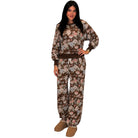 A woman modeling a matching two-piece lounge set featuring a brown and beige floral print sweatshirt and jogger pants, paired with tan slippers, against a plain white background.