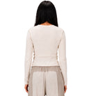 A woman shown from the back wearing a ribbed long-sleeve knit top in a light cream color and light beige textured pants, set against a plain white background.