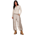 A woman modeling a cream long-sleeve henley top and beige wide-leg patchwork pants with brown lace-up ankle boots, set against a plain white background.