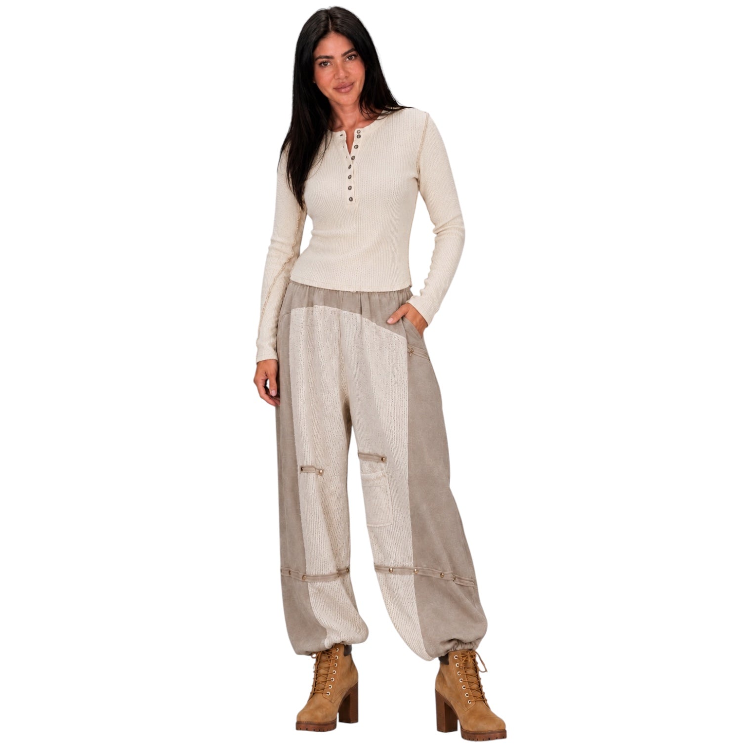A woman modeling a cream long-sleeve henley top and beige wide-leg patchwork pants with brown lace-up ankle boots, set against a plain white background.