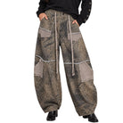 A woman modeling a pair of loose, wide-leg patchwork pants in a brown and beige animal print with a beige drawstring, paired with a black off-the-shoulder long-sleeve top and black shoes, against a plain white background.