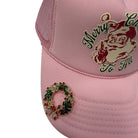 A light pink trucker hat featuring a red and green embroidered Santa Claus graphic on the front and a red and green rhinestone Christmas wreath embellishment on the brim.