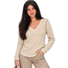 A woman modeling a beige waffle-knit long-sleeve sweater with white lace trim along the V-neck, cuffs, and hem, paired with khaki cargo pants against a plain white background.