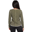 A woman viewed from the back wearing a textured olive green and black houndstooth knit sweater with cream-colored trim and a decorative button detail at the back neckline, paired with black jeans against a plain white background.