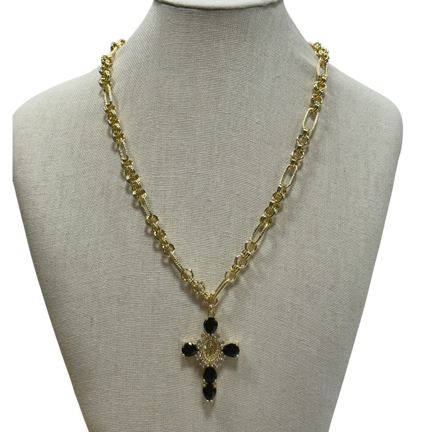 A gold-tone chain necklace with a cross pendant featuring black stones, displayed on a beige fabric jewelry bust against a white background.