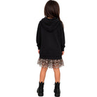 A child model shown from the back wearing a black oversized hoodie, a leopard-print ruffled mini skirt, and black platform ankle boots against a plain white background.
