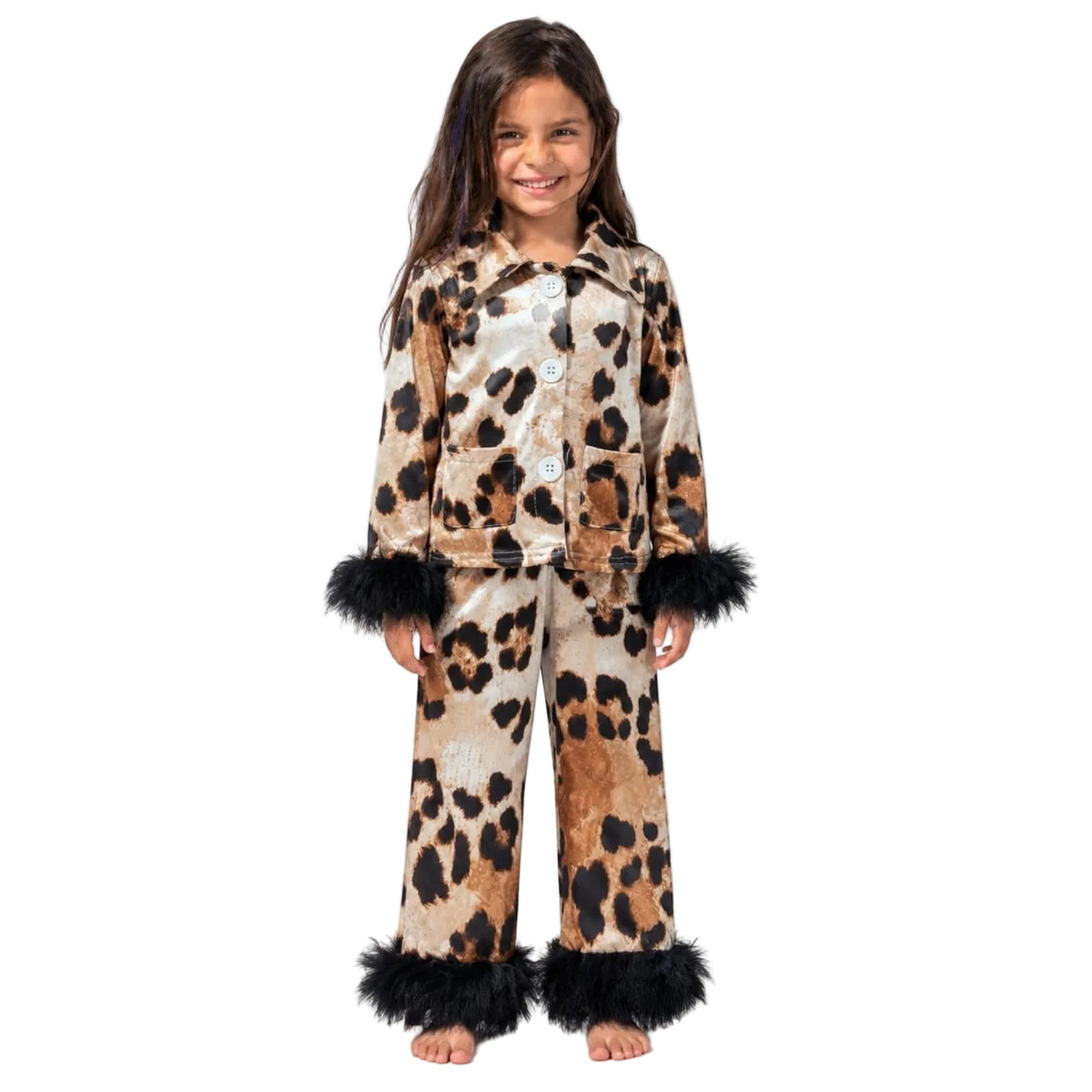 A young girl stands barefoot against a plain white studio background wearing a matching two-piece pajama set with a leopard print pattern and black faux-fur trim at the cuffs and hem.