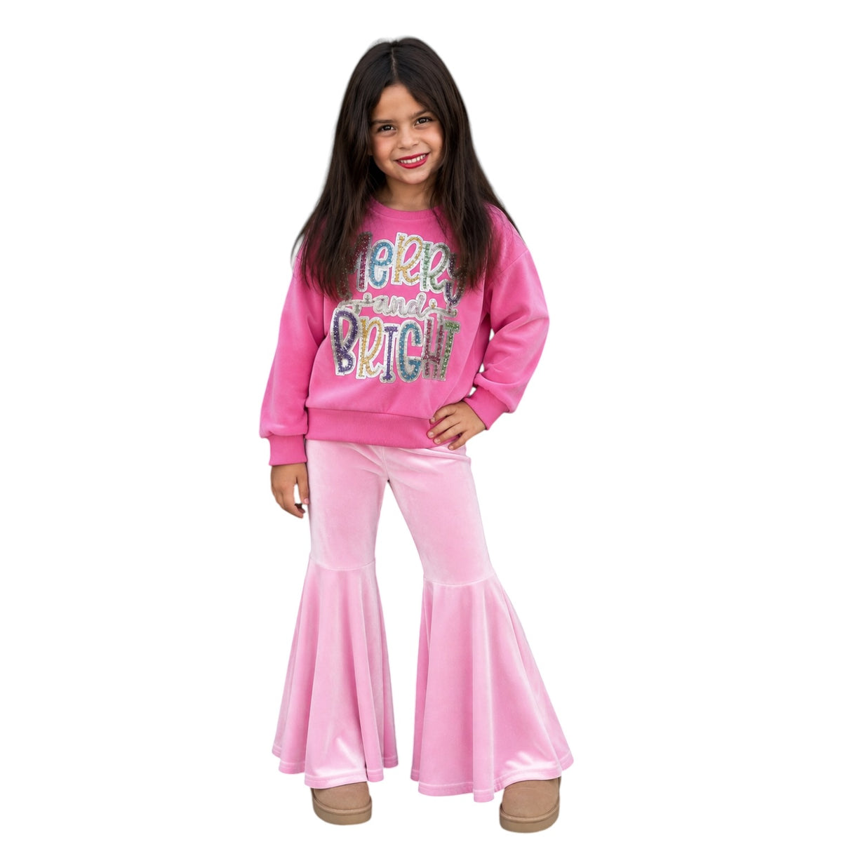 A young girl modeling a two-piece pink outfit consisting of a long-sleeve sweatshirt with a colorful 'BE RICH' graphic and matching pink flared pants, set against a plain white background.