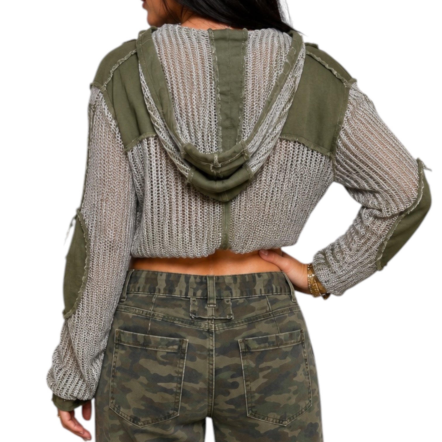 A woman modeling a cropped button-front knit top with striped gray and olive green panels, green patch pockets, and green elbow patches, paired with camouflage pants, against a plain white background.