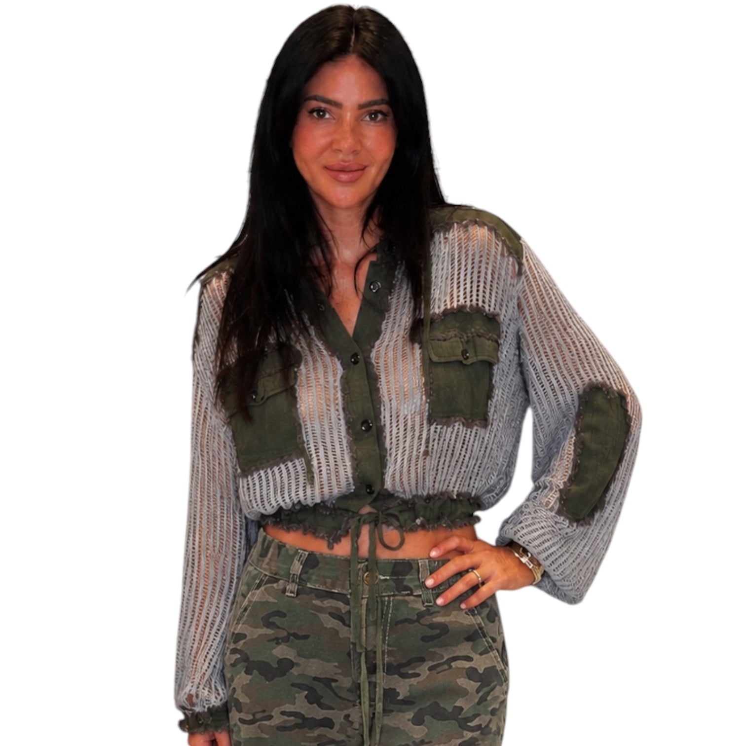 A woman modeling a cropped button-front knit top with striped gray and olive green panels, green patch pockets, and green elbow patches, paired with camouflage pants, against a plain white background.