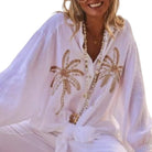 Woman wearing a white cover-up with gold palm tree designs on a white background