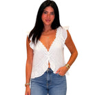Woman wearing a white sleeveless top with ruffled shoulders and blue jeans on a white background