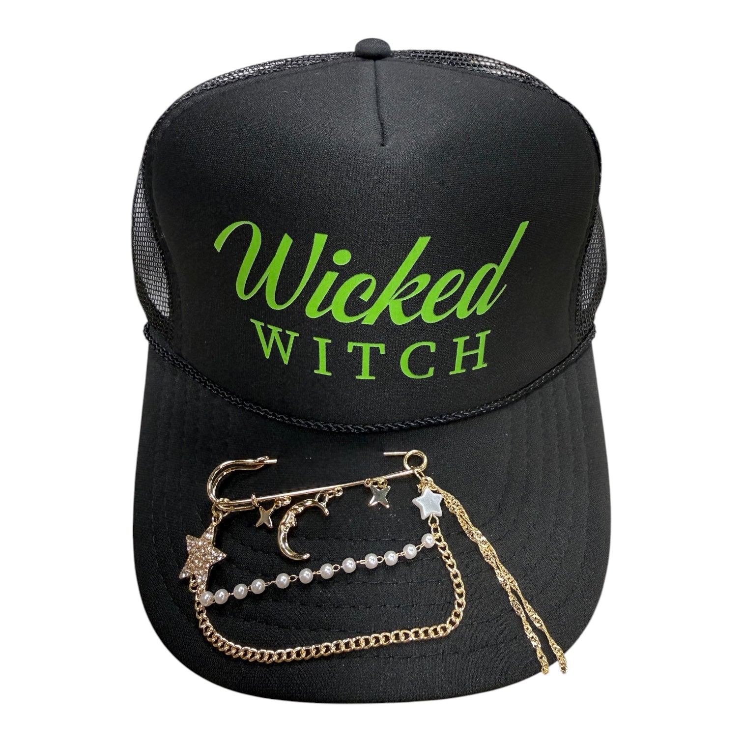 A black trucker hat with 'Wicked Witch' printed in neon green on the front, styled with a gold chain brooch featuring star and moon charms and a pearl bead chain on the brim.