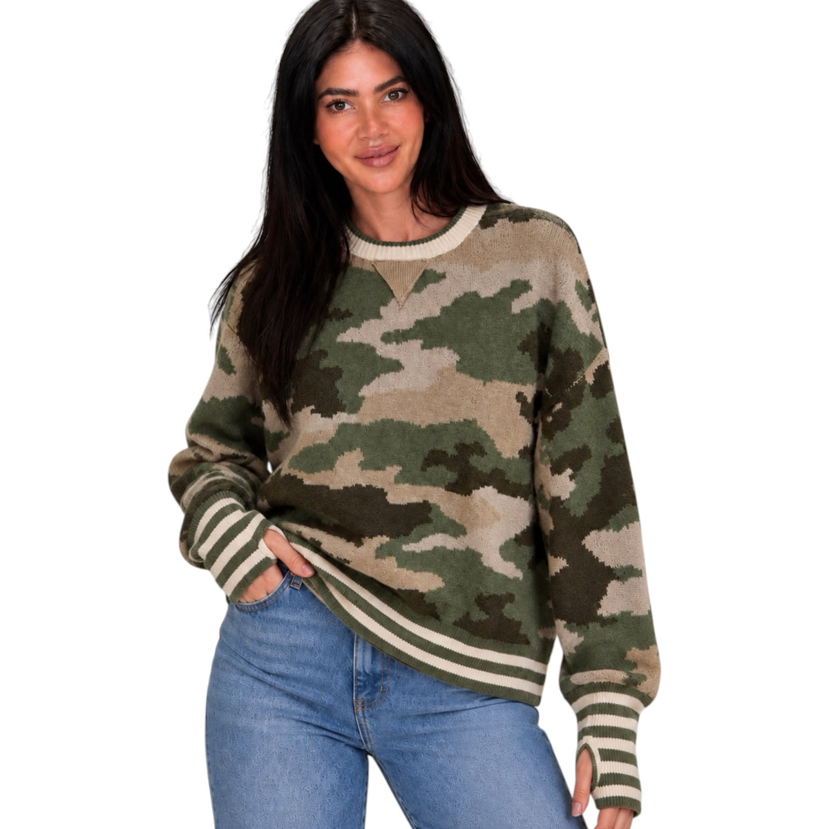 A woman wearing a long-sleeve crewneck sweater with a green, brown, and beige camouflage pattern and striped ribbed cuffs and hem, paired with blue jeans against a plain white background.