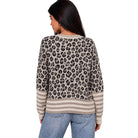A woman shown from the back wearing a beige and black leopard print sweater with striped cuffs and hem, paired with blue jeans, against a plain white background.