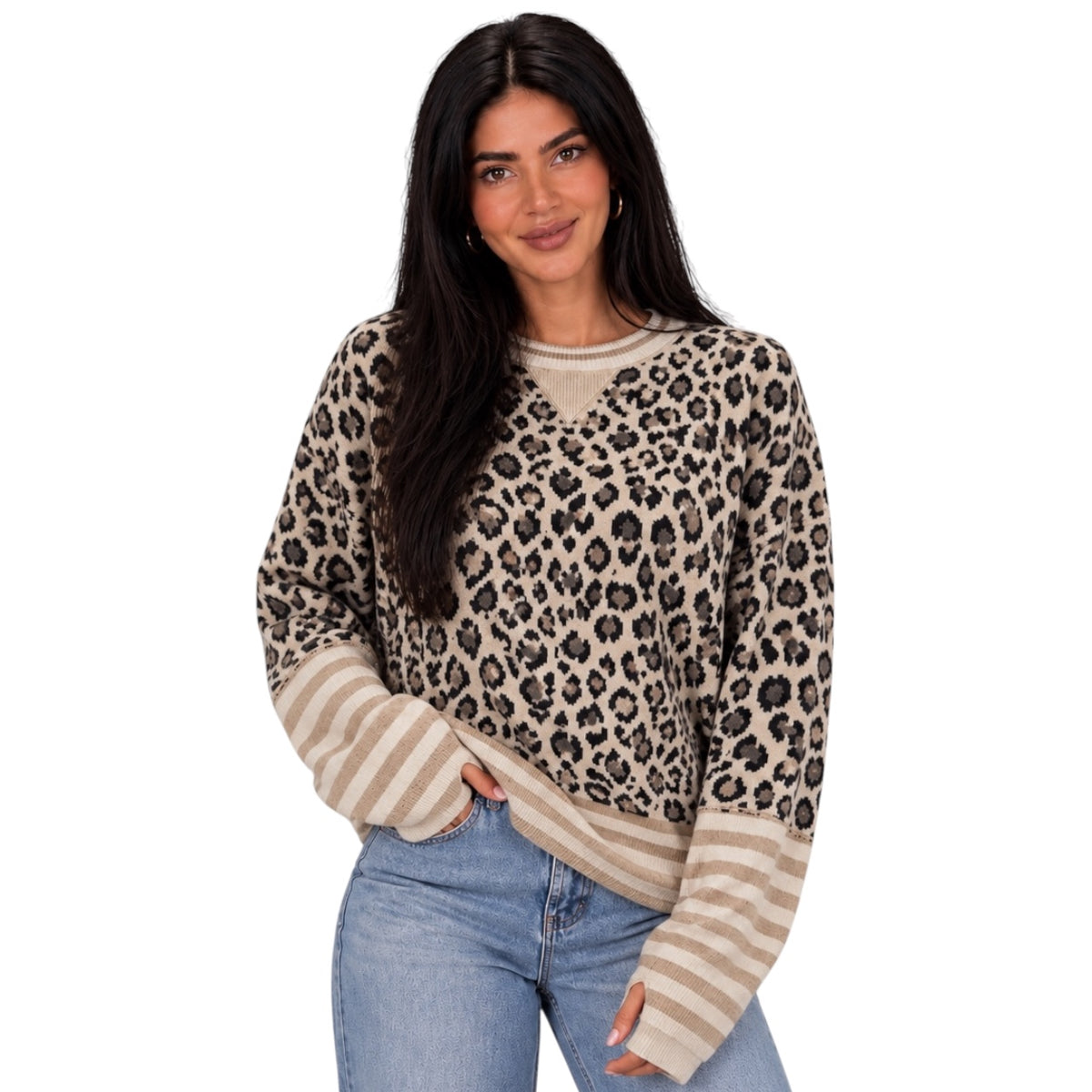 A woman modeling a long-sleeve knit sweater with a beige and black leopard print body and solid beige striped sleeves, paired with blue jeans against a plain white background.