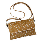 A small crossbody clutch bag made of tan cowhide with white irregular spots, featuring a matching tan strap and whipstitched edges, shown on a plain white background.