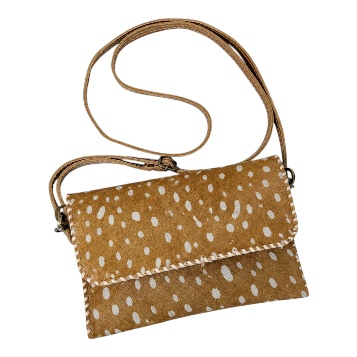 A small crossbody clutch bag made of tan cowhide with white irregular spots, featuring a matching tan strap and whipstitched edges, shown on a plain white background.