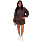 A woman modeling a matching brown zip-up jacket and shorts set, paired with white sneakers, against a plain white background.