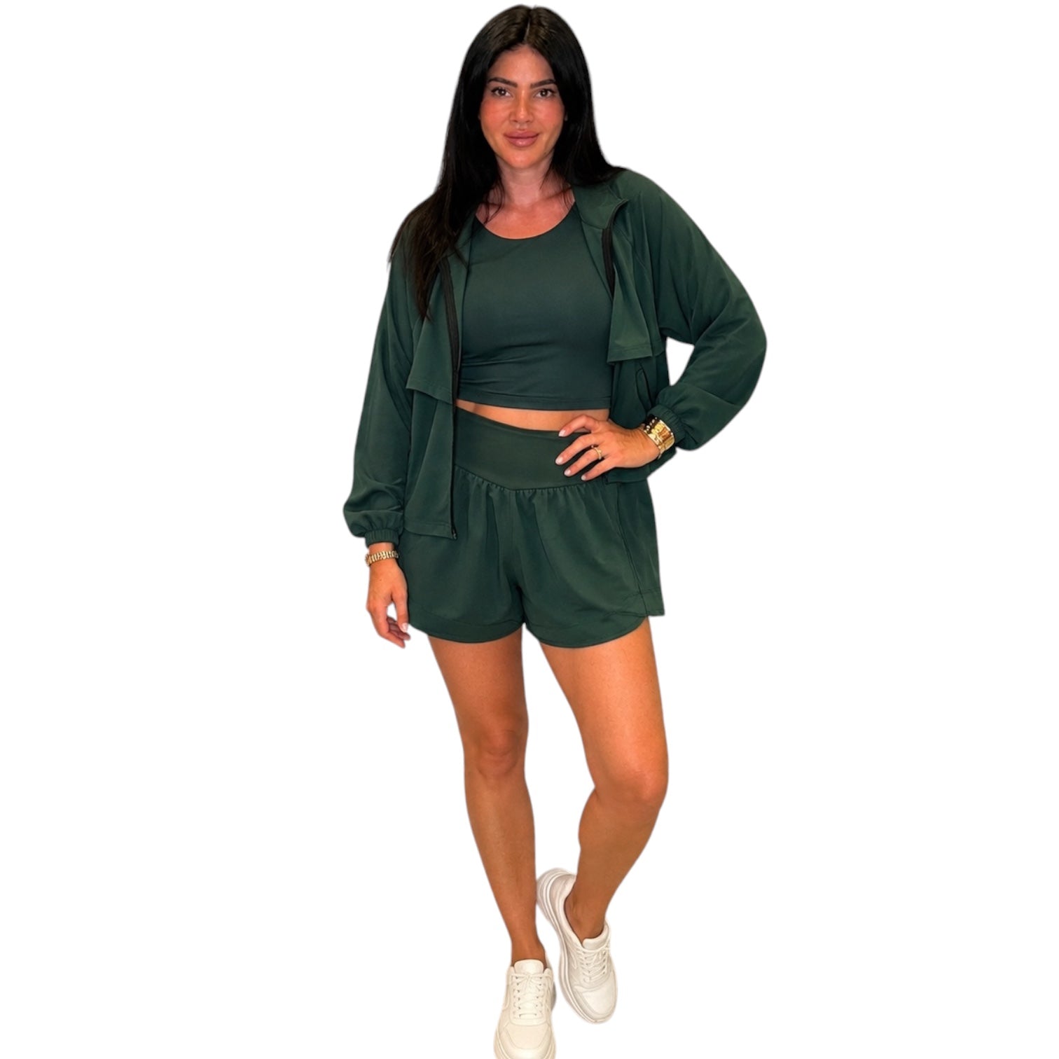 A woman modeling a dark green two-piece lounge set consisting of a cropped tank top and matching shorts, styled with a matching open-front long-sleeve hoodie jacket and white sneakers against a plain white background.