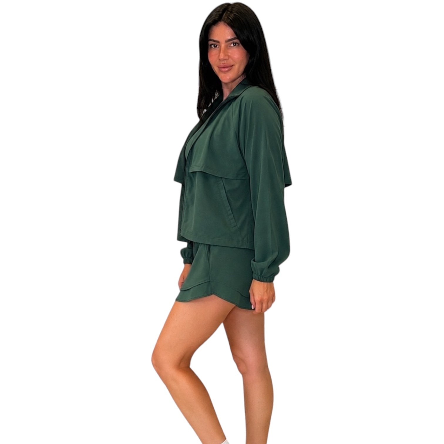 A woman modeling a dark green two-piece lounge set consisting of a long-sleeve cropped top with layered ruffle details and matching shorts, set against a plain white background.