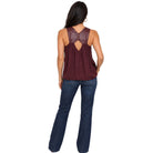 A woman shown from the back wearing a sleeveless maroon top with a faux-leather back panel and keyhole cutout, paired with dark blue jeans, against a plain white background.