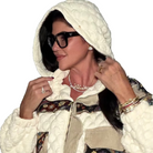 Woman wearing a white hooded jacket with a patterned inner lining, black glasses, and jewelry.