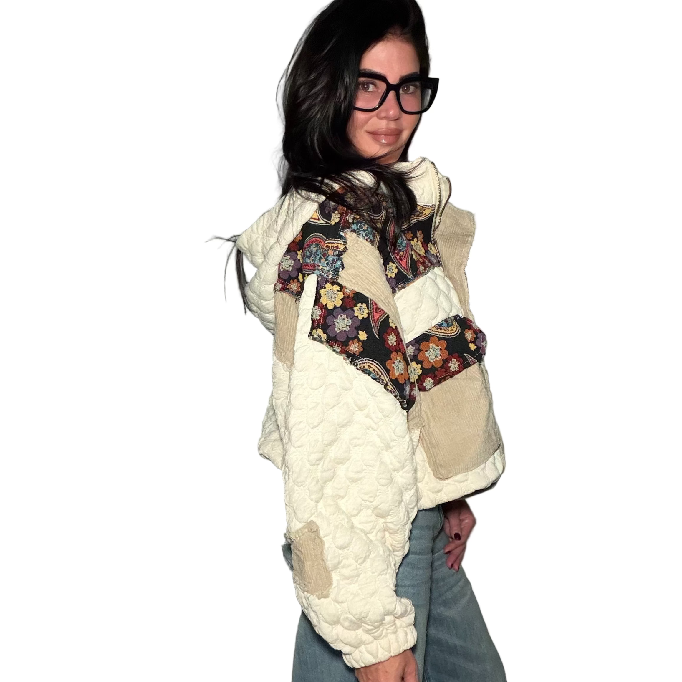 Person wearing a white quilted jacket with floral patterned accents and blue jeans against a plain wall.