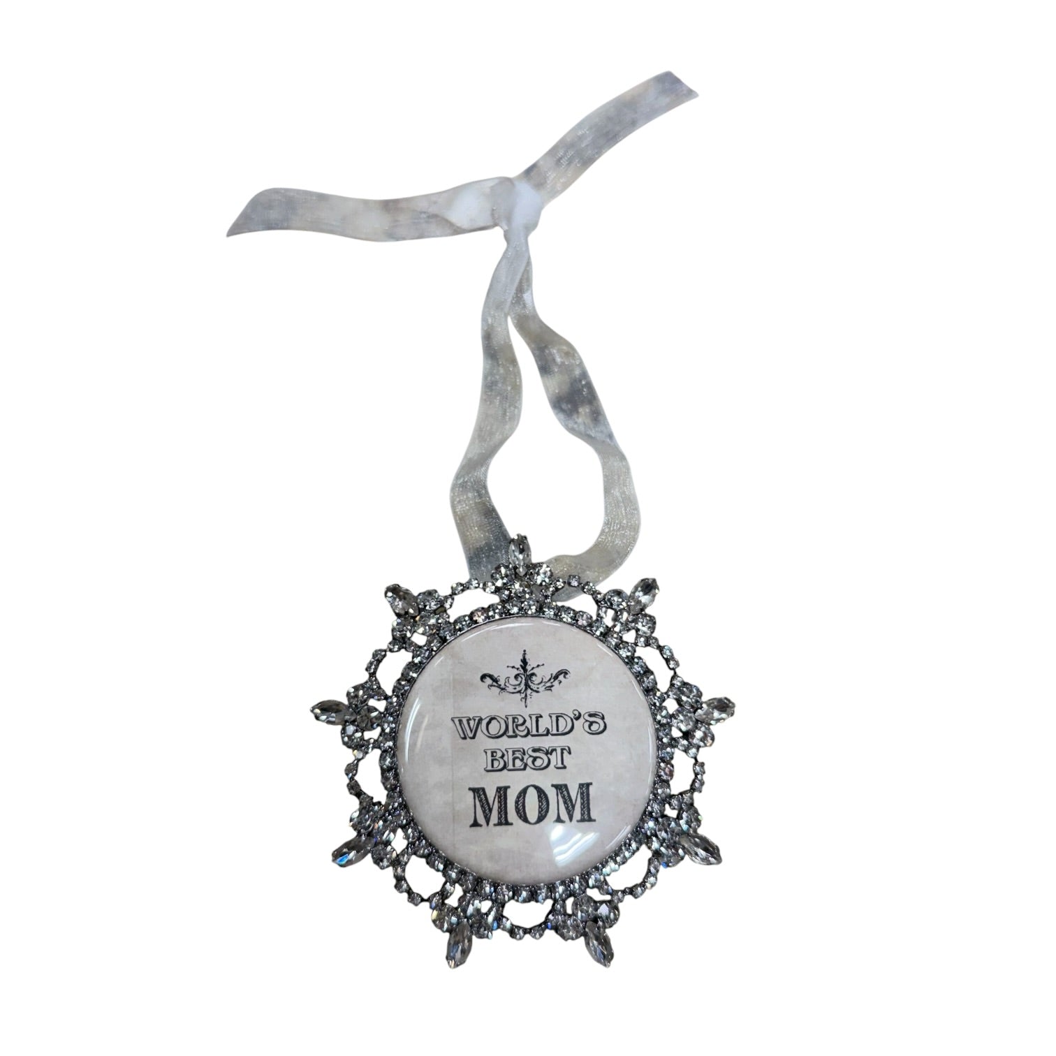 A decorative hanging ornament with a silver filigree-style frame and a white oval center that reads 'WORLD'S BEST MOM.' The ornament hangs from a sheer silver ribbon against a plain white background.