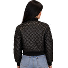 A woman viewed from the back wearing a black quilted bomber jacket with a diamond-stitched pattern, paired with light blue jeans, against a plain white background.