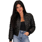 A woman modeling a black quilted faux-leather bomber jacket with silver zippers, worn over a black top and blue jeans against a plain white background.