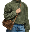 A person wearing an olive green corduroy jacket and blue jeans, carrying a brown faux-fur crossbody bag with a tan strap.