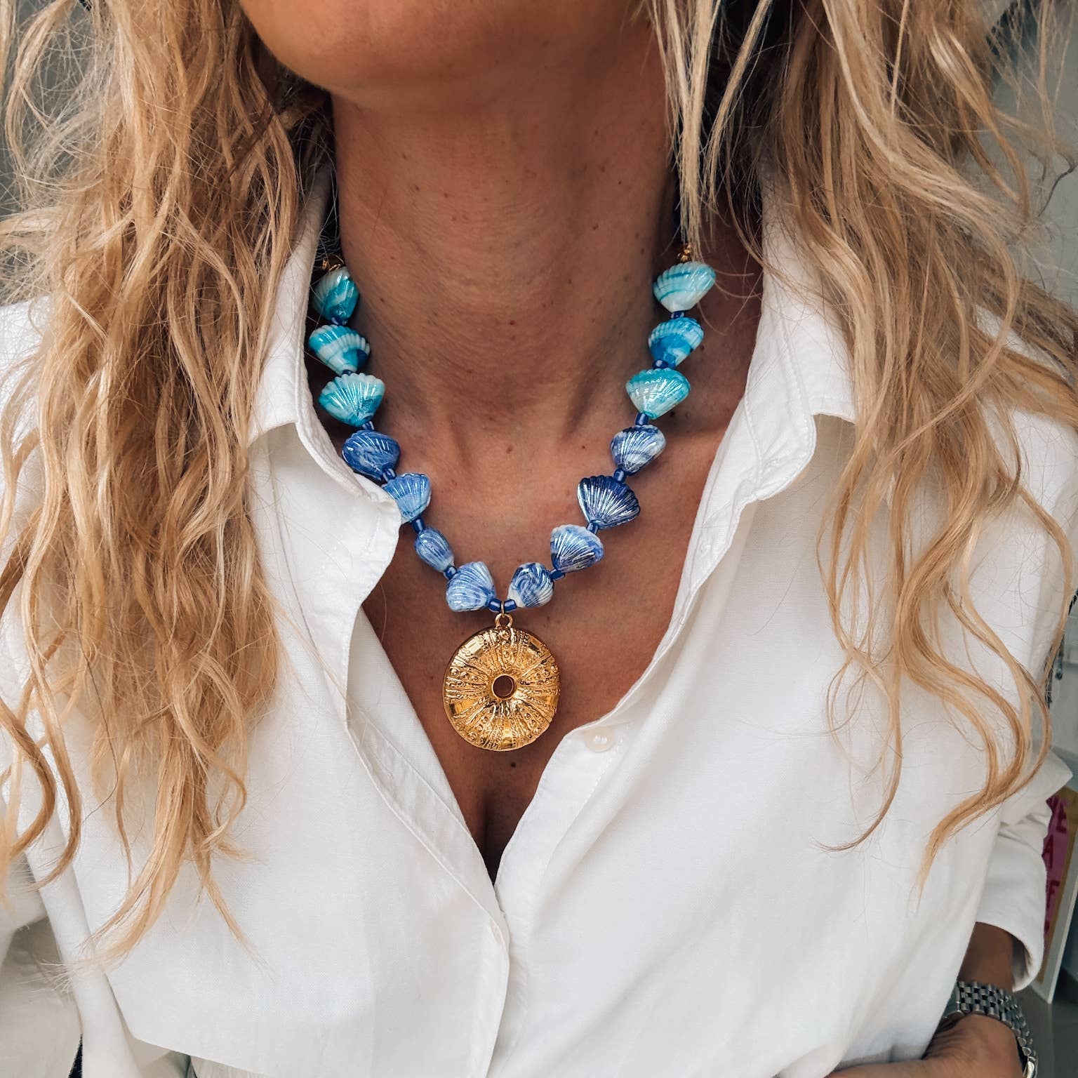 Gold large urchin statement necklace featuring blue glass scallop shells, perfect for summer beachwear.