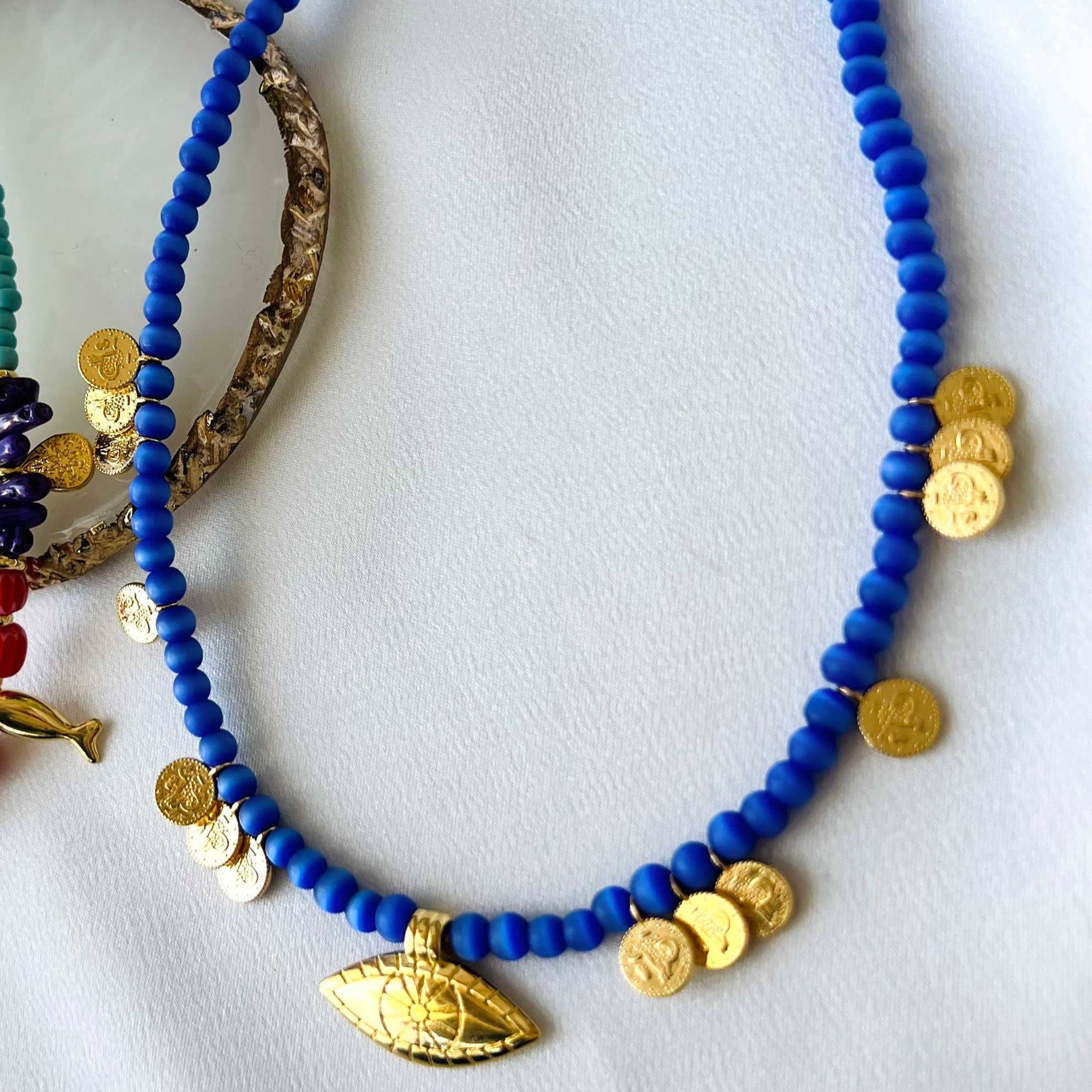 Multi charm summer necklace featuring blue glass beads and goldplated accents, 35cm with adjustable length.