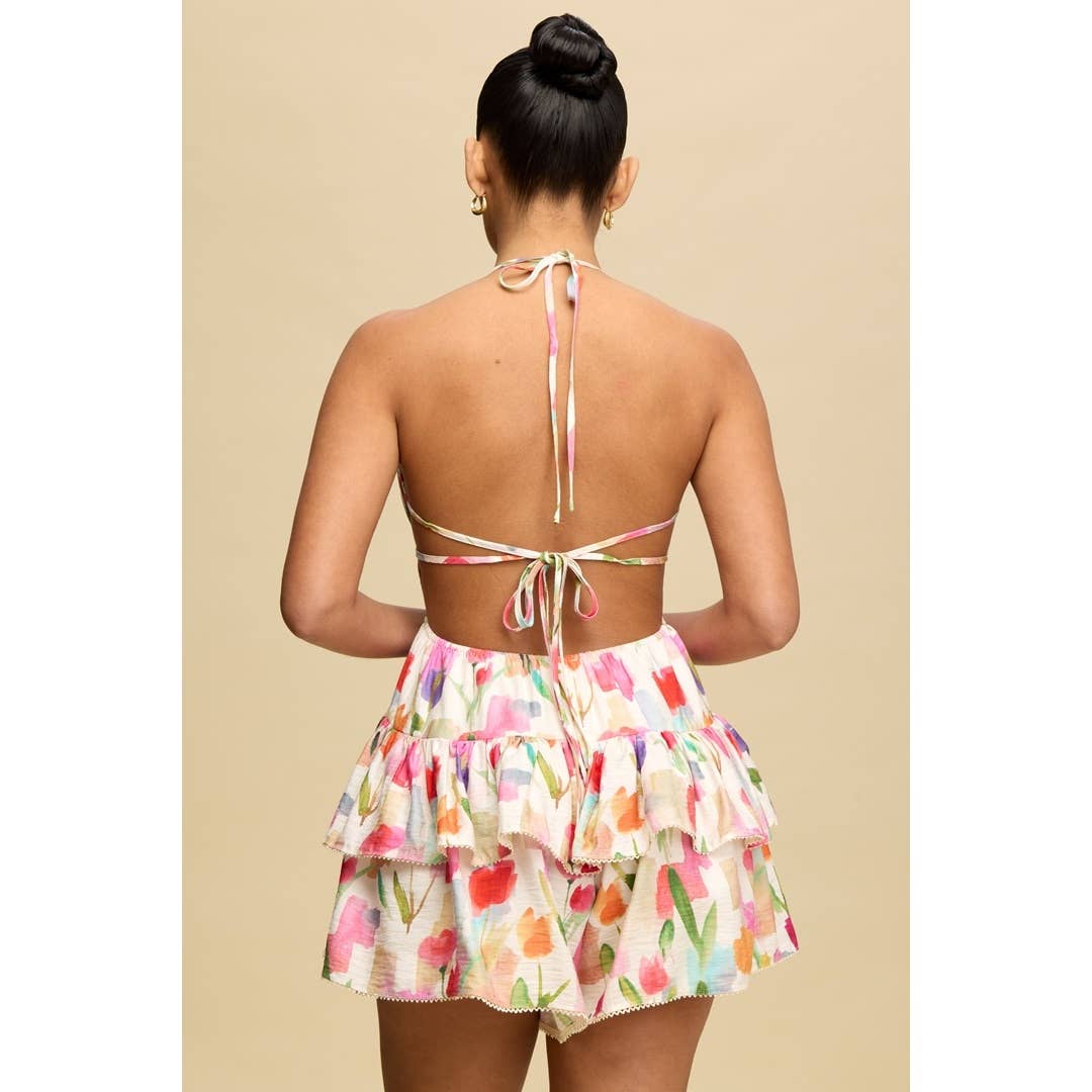 Back view of a woman wearing a colorful Calla Ruffle Hem Romper with flirty ruffle details.
