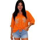 Woman wearing an orange shirt with palm tree designs and denim shorts on a white background