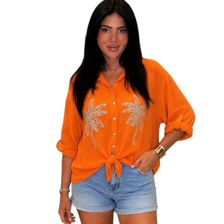 Woman wearing an orange shirt with palm tree designs and denim shorts on a white background